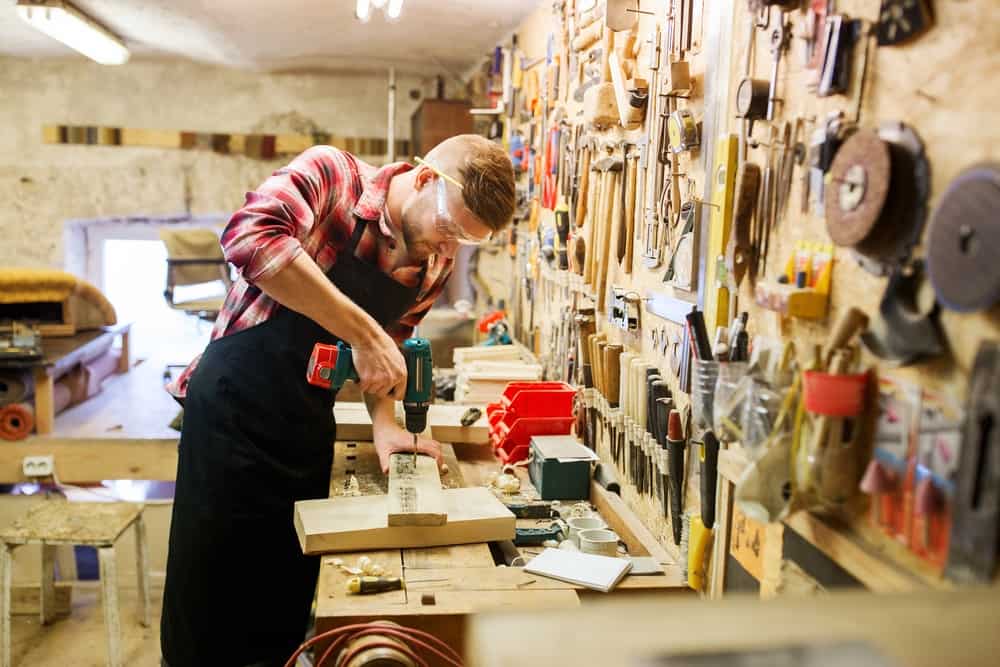 carpenter with drill drilling plank at workshop